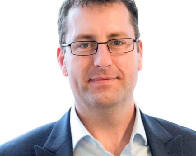 Professional headshot of a person wearing glasses, with short hair, a light blue shirt, and a dark blazer. They are smiling slightly and looking directly at the camera against a plain white background. ©Mobysoft