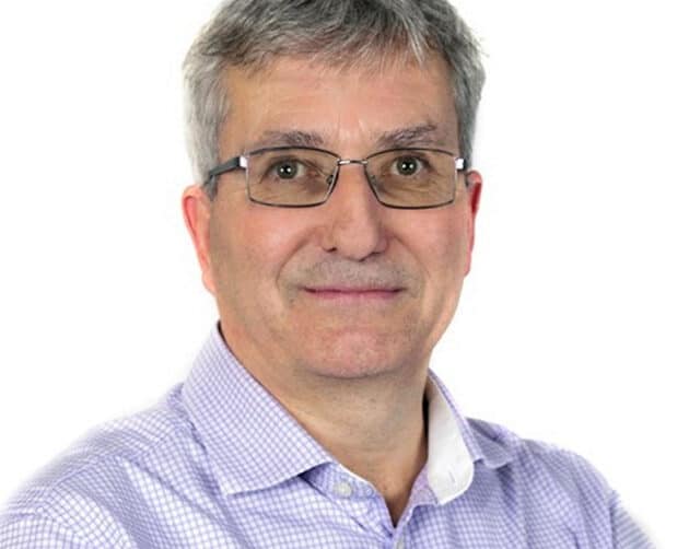 A man with short gray hair and glasses is smiling at the camera. He is wearing a light purple checkered shirt against a white background. ©Mobysoft