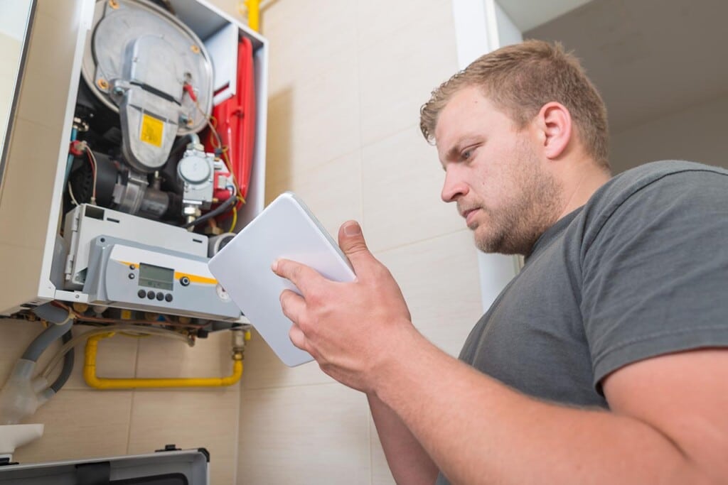 A man in a gray t-shirt is using RepairSense on his tablet as he examines the open, wall-mounted boiler. Exposed internal components and yellow pipes are visible, showcasing the intricate details he's navigating with ease. ©Mobysoft