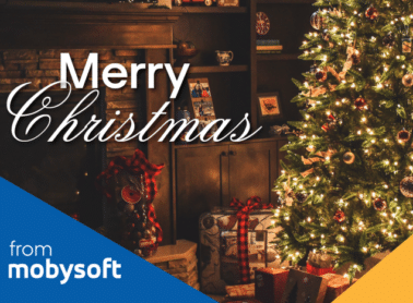 A warmly lit Christmas tree with ornaments stands beside a fireplace. Wrapped gifts are placed nearby. "Merry Christmas" text is overlaid in white. The bottom left corner features a blue section with "from mobysoft" written in white. ©Mobysoft