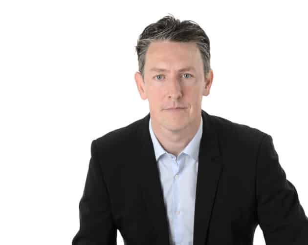 A man with short dark hair, wearing a black suit and a light blue shirt, sits against a white background. He looks directly at the camera with a neutral expression. ©Mobysoft