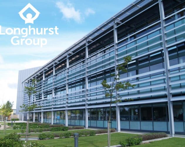 Modern office building with large glass windows and a grid-like facade. "Longhurst Group" logo is visible in the top left corner. The foreground features a well-maintained lawn with young trees and small shrubs under a partly cloudy sky. ©Mobysoft