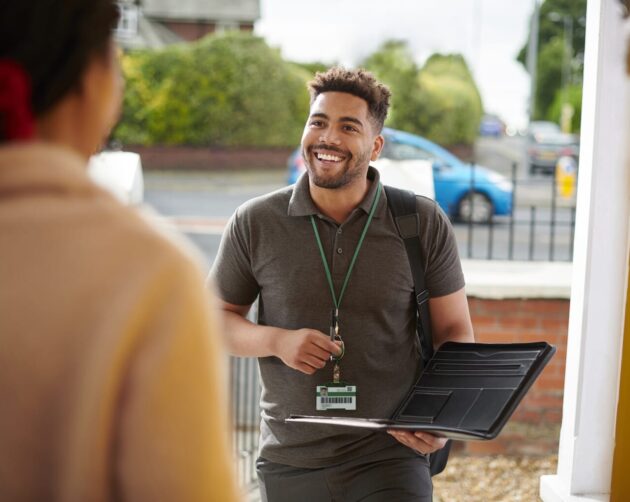 A smiling man with a laptop, ID badge, and backpack stands at a doorstep, actively engaging in resident engagement with another person. Surrounded by greenery and a street in the background, he embodies approachable professionalism outdoors. ©Mobysoft