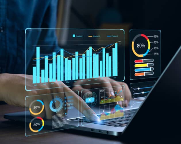 Hands interact with a laptop featuring holographic charts and graphs. Displays include bar graphs, pie charts, and percentage data, each showing diverse analytics essential for data-driven social housing repairs, reflecting advanced data visualization or financial analysis. ©Mobysoft